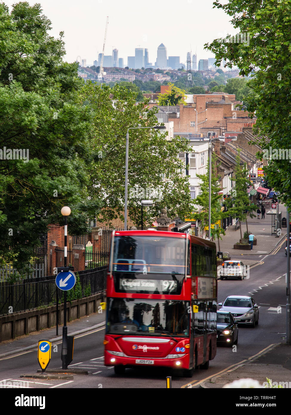 London, England, UK - June 1, 2019: A London double-decker bus climbs Old Church Road in Chingford, with the skyline of London's Docklands business di Stock Photo