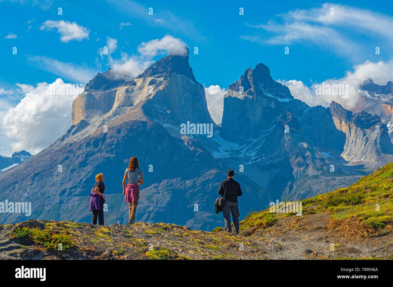A group of three tourists looking upon the Andes peaks of Cuernos del Paine in Chilean Patagonia. Unsharp foreground, sharp background. Stock Photo