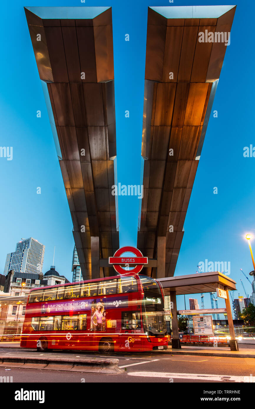 London, England, UK - May 28, 2019: Buses pass under the distinctive cantilevered roof of Vauxhall Bus Station in South London at dusk. Stock Photo
