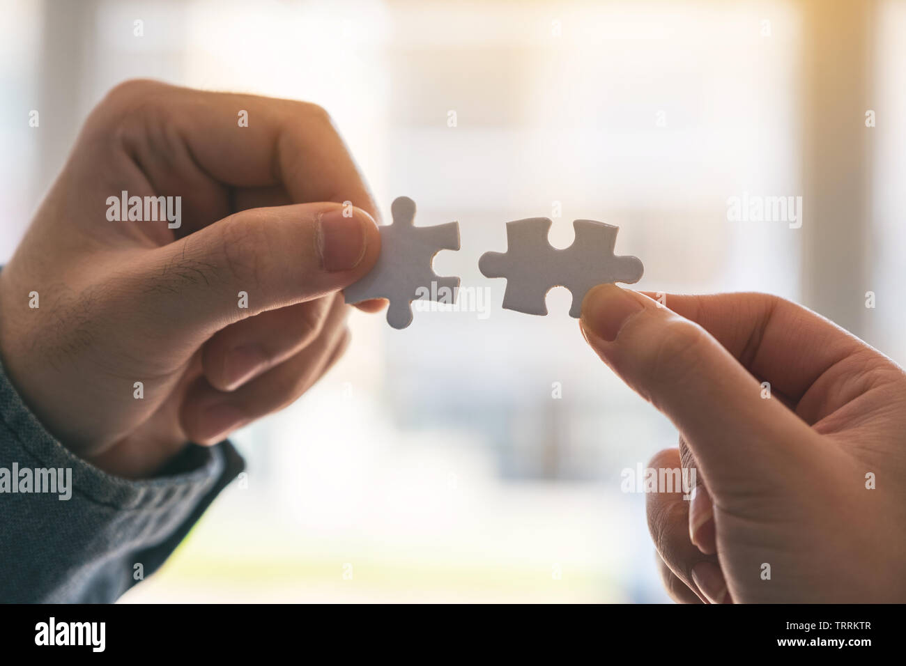 Closeup image of two hands holding and putting a piece of white jigsaw puzzle together Stock Photo