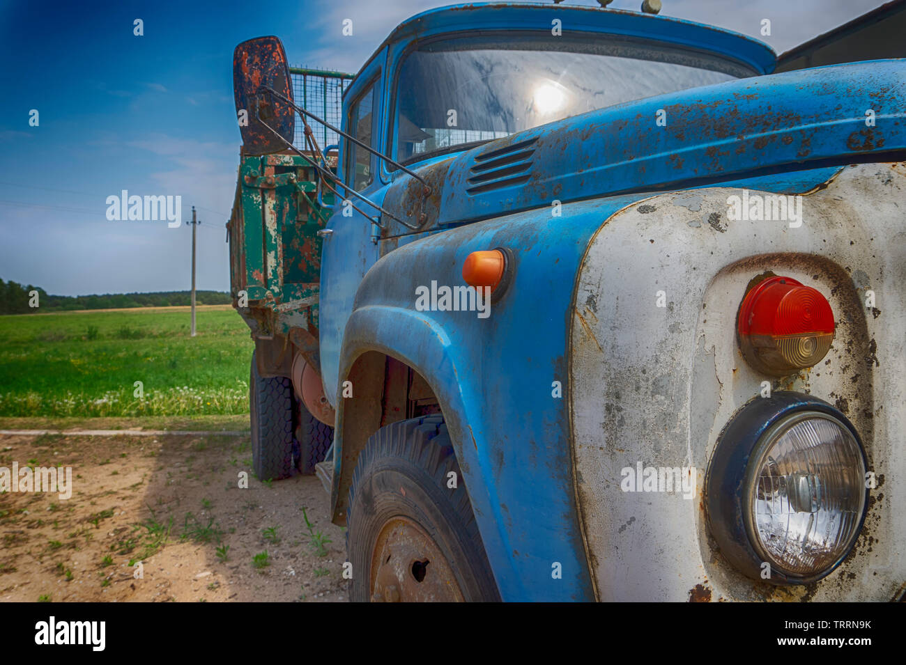 Old rusting truck or lorry outdoors in a field under a cloudy blue sky ...