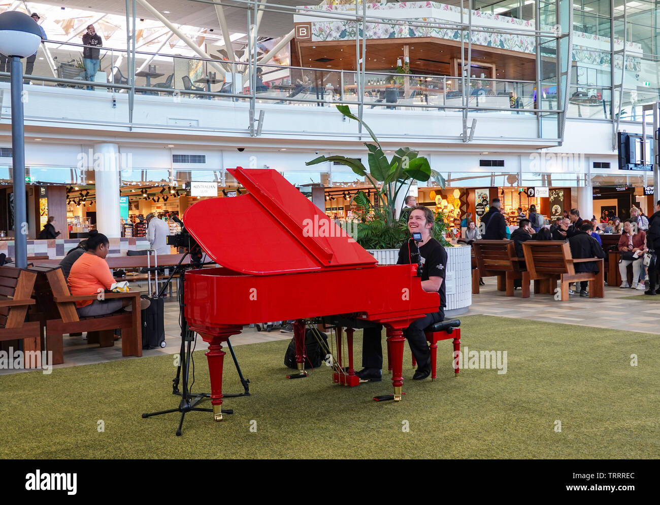 Musician playing on a red grand piano at Brisbane Airport Departures area, Queensland, QLD, Australia Stock Photo