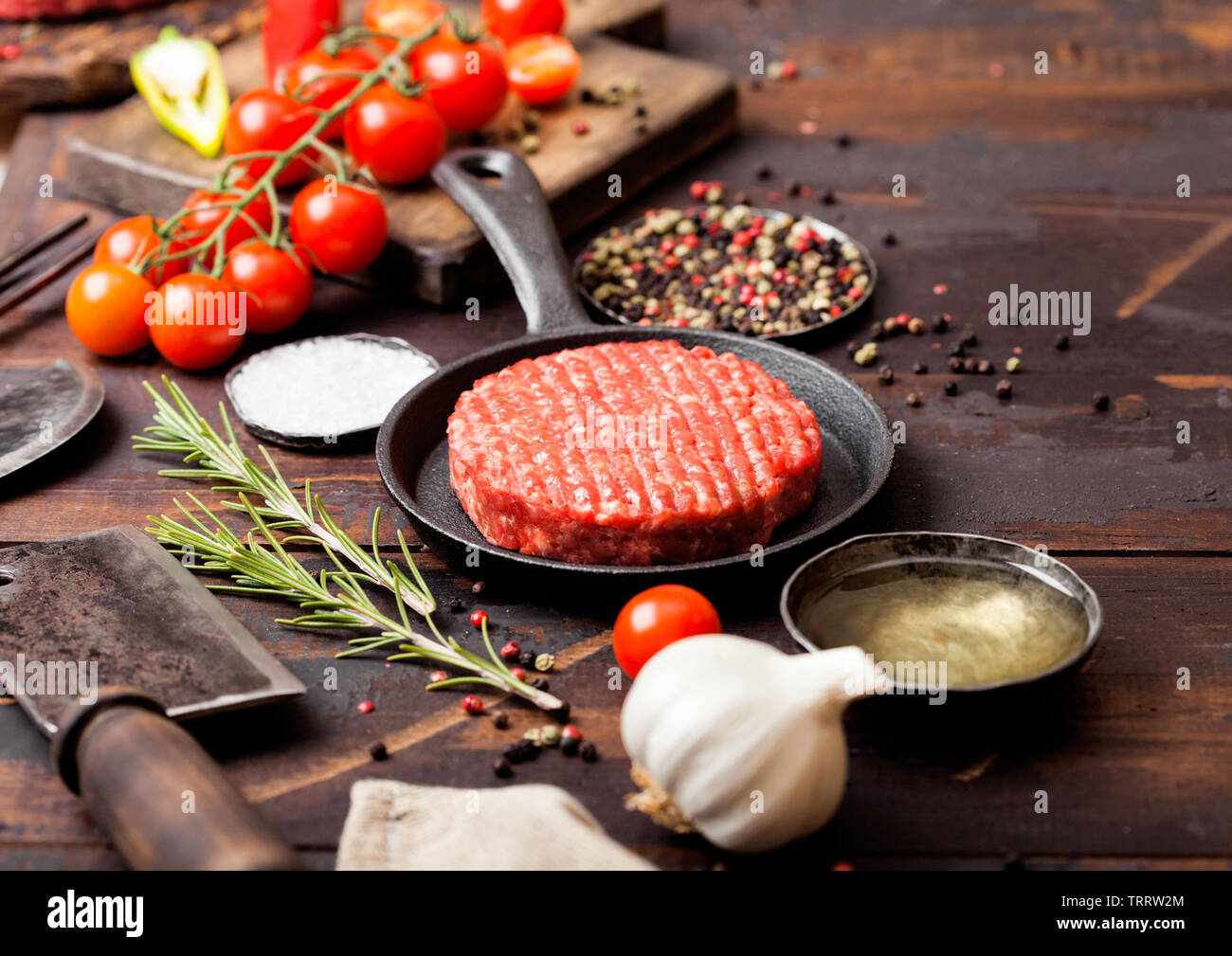 Fresh raw minced homemade farmers grill beef burger in frying pan with spices and herbs and meat hatchet on wooden board. Stock Photo