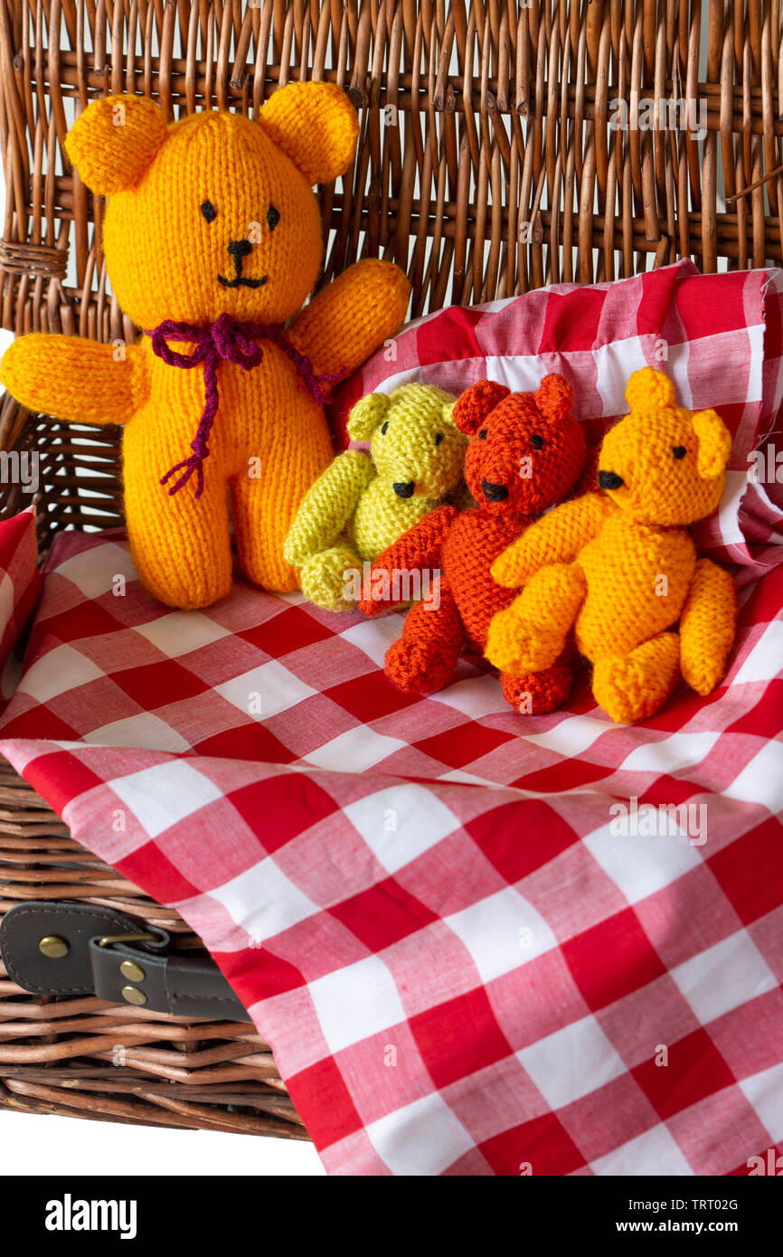 Knitted teddy bear toys on gingham fabric material in a wicker picnic
