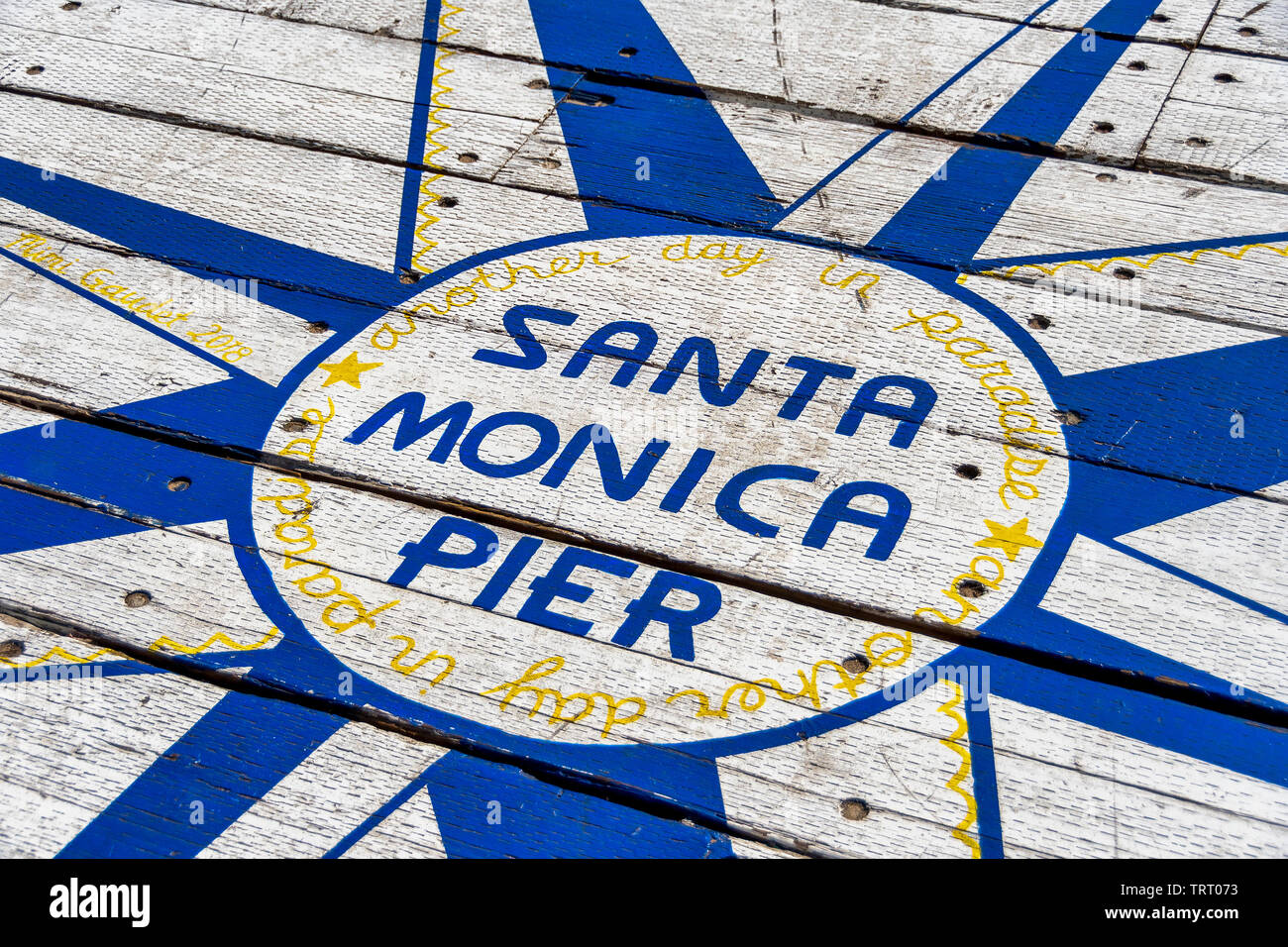 Sign on the ground says Santa Monica Pier, another day in paradise. The sign is located at the end of Santa Monica pier, in southern California. Stock Photo