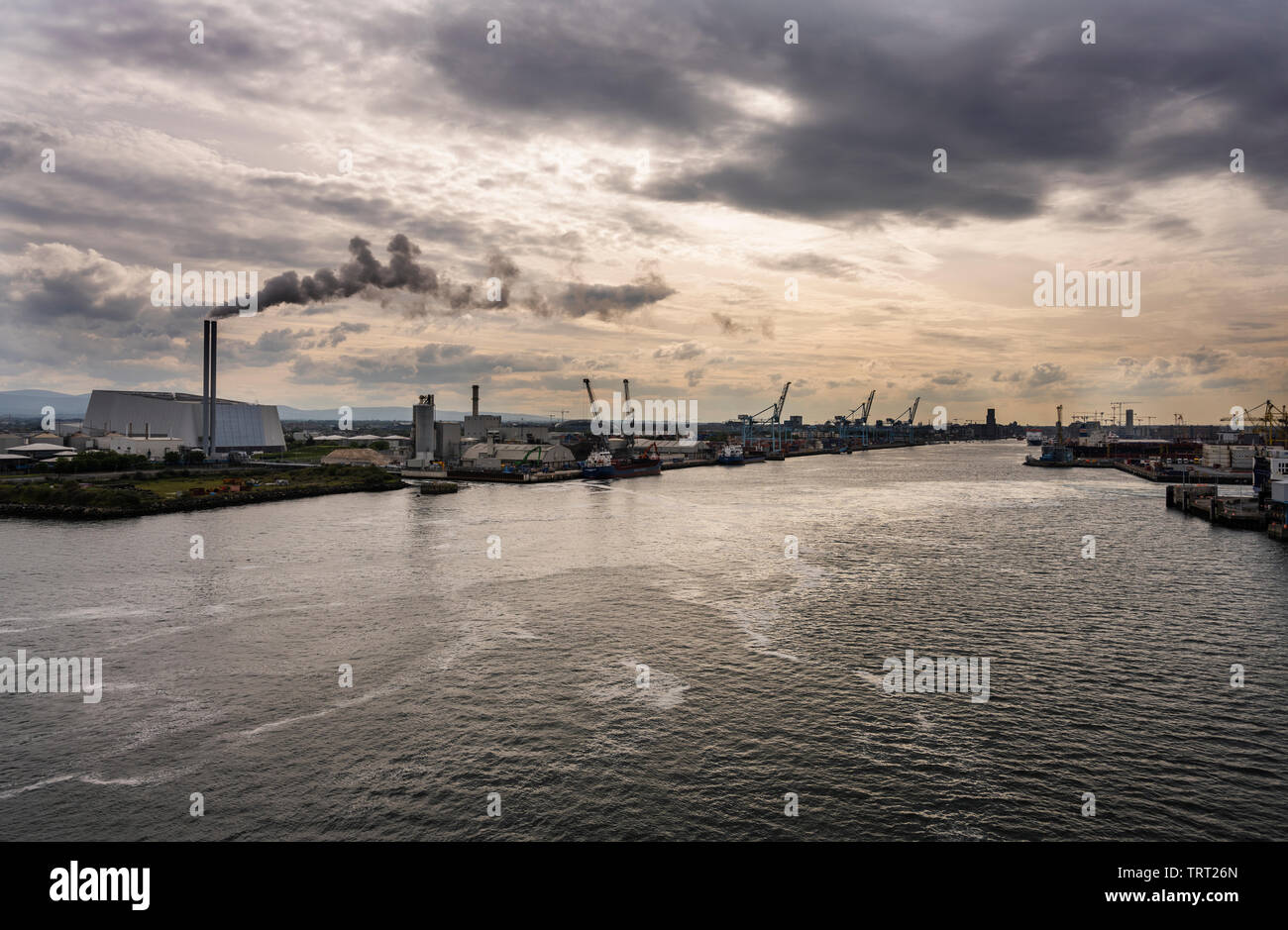 The mouth of the River Liffey, Dublin Port, Ireland, with the Dublin Waste-to-Energy Facility incinerator emitting a plume against a dark sky Stock Photo