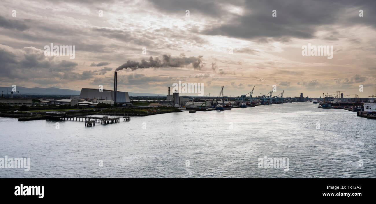 The mouth of the River Liffey, Dublin Port, Ireland, with the Dublin Waste-to-Energy Facility incinerator emitting a plume against a dark sky Stock Photo