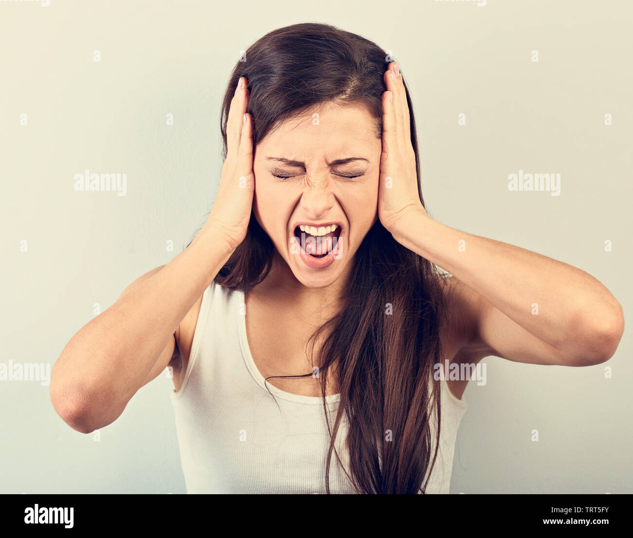 Anger young business woman strong screaming with wild open mouth and holding head the hands on blue background. Closeup toned portrait Stock Photo