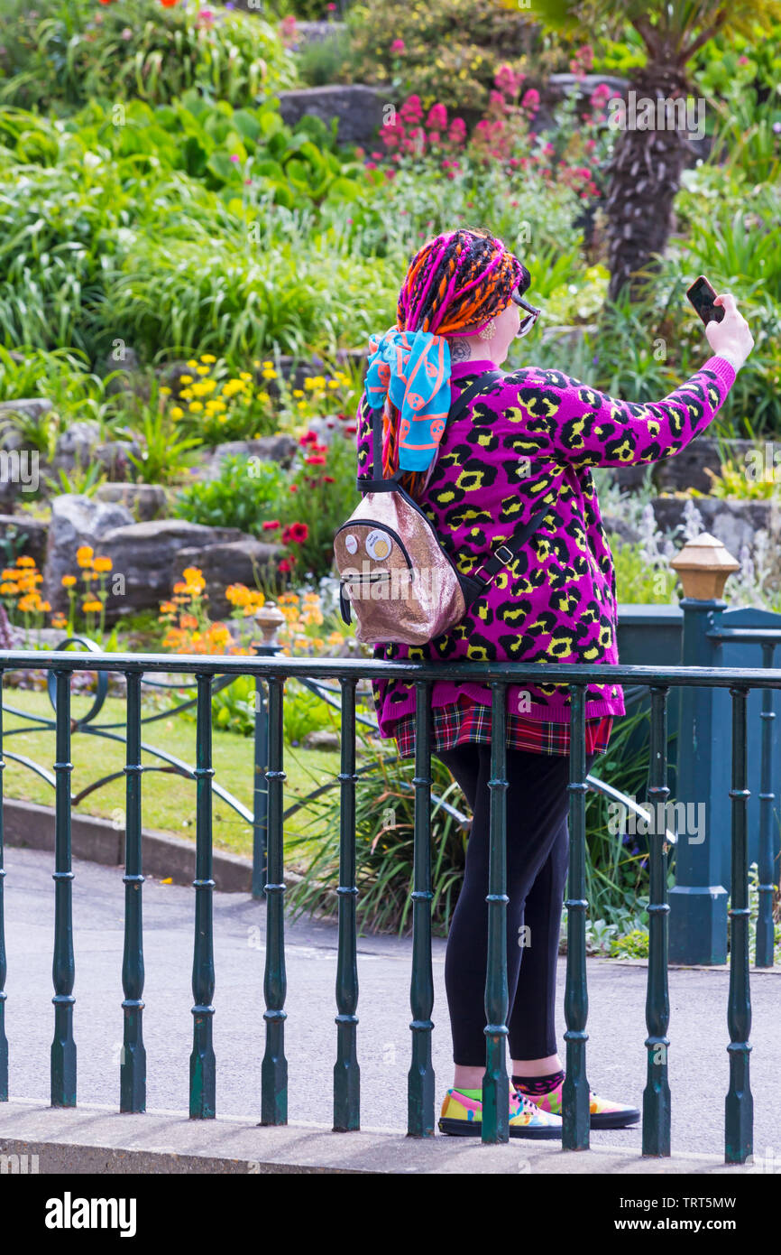 Woman in colourful jumper taking selfie in Bournemouth Lower Gardens at Bournemouth, Dorset UK in June Stock Photo