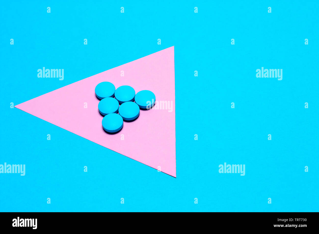 blue tablets laid out in the form of a triangle or an arrow on a paper background of blue and pink. Medication and prescription pills minimalistic fla Stock Photo