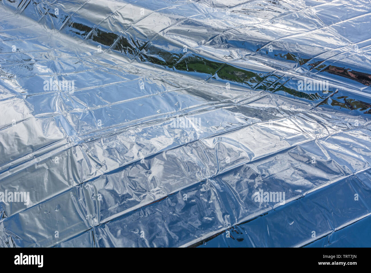 Unfolded Mylar metalized space blanket reflecting blue sky and clouds