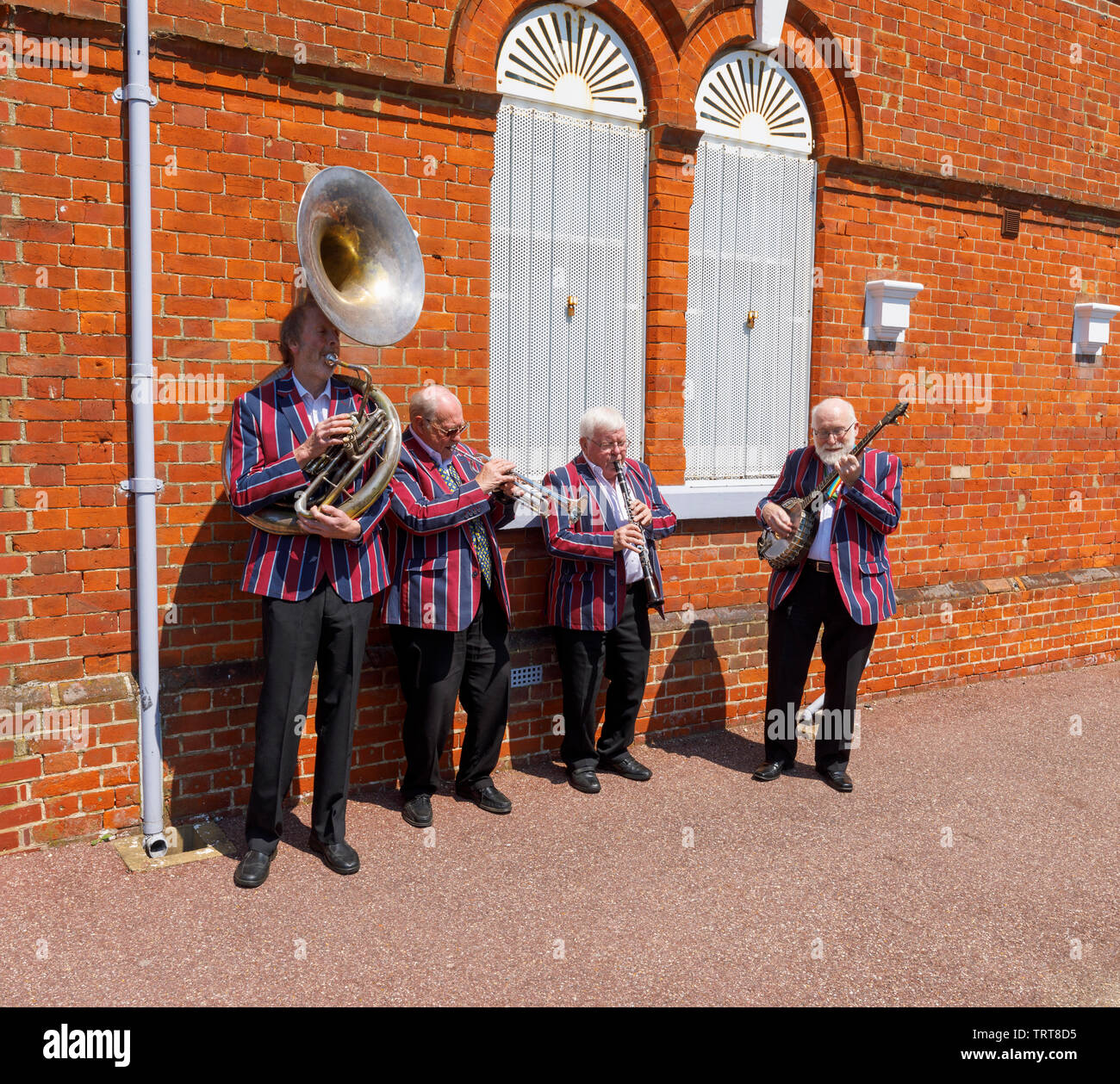 Elderly musicians from the Belmond Venice Simplon Orient Express in striped blazers entertain and perform at Folkestone West railway station, Kent Stock Photo