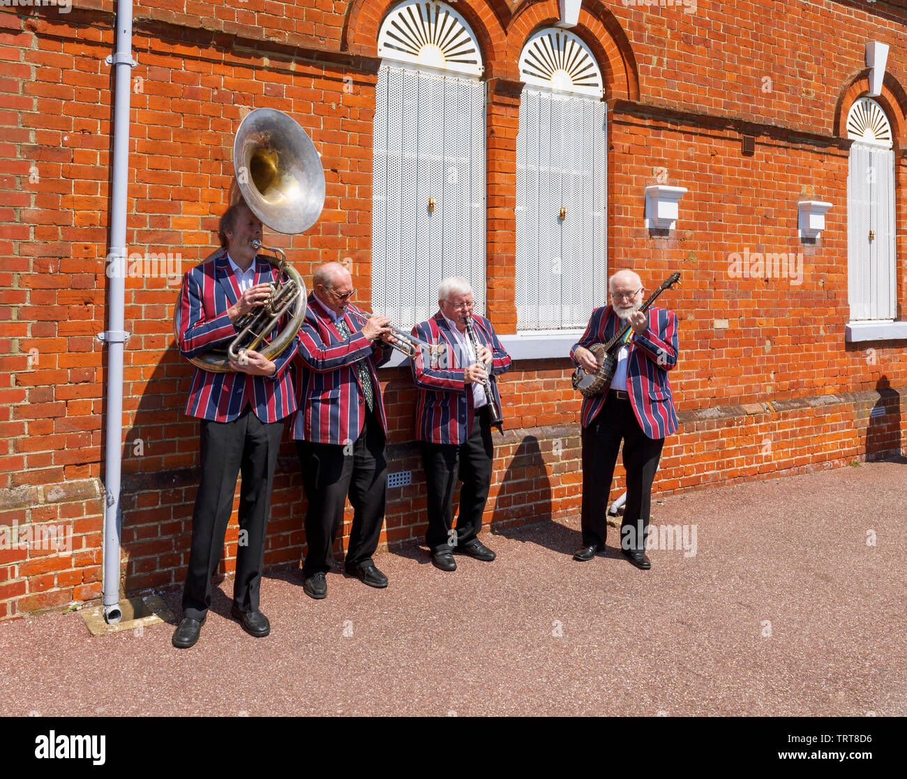 Elderly musicians from the Belmond Venice Simplon Orient Express in striped blazers entertain and perform at Folkestone West railway station, Kent Stock Photo