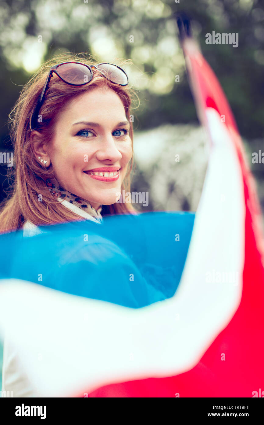 Happy young woman with smile holding flag of Netherlands in park, depth of field Stock Photo