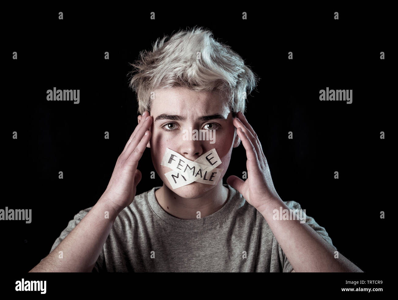 Transgender teenager with mouth sealed on tape with words male and female written in social taboo of gender diversity concept. Trans boy not able to c Stock Photo