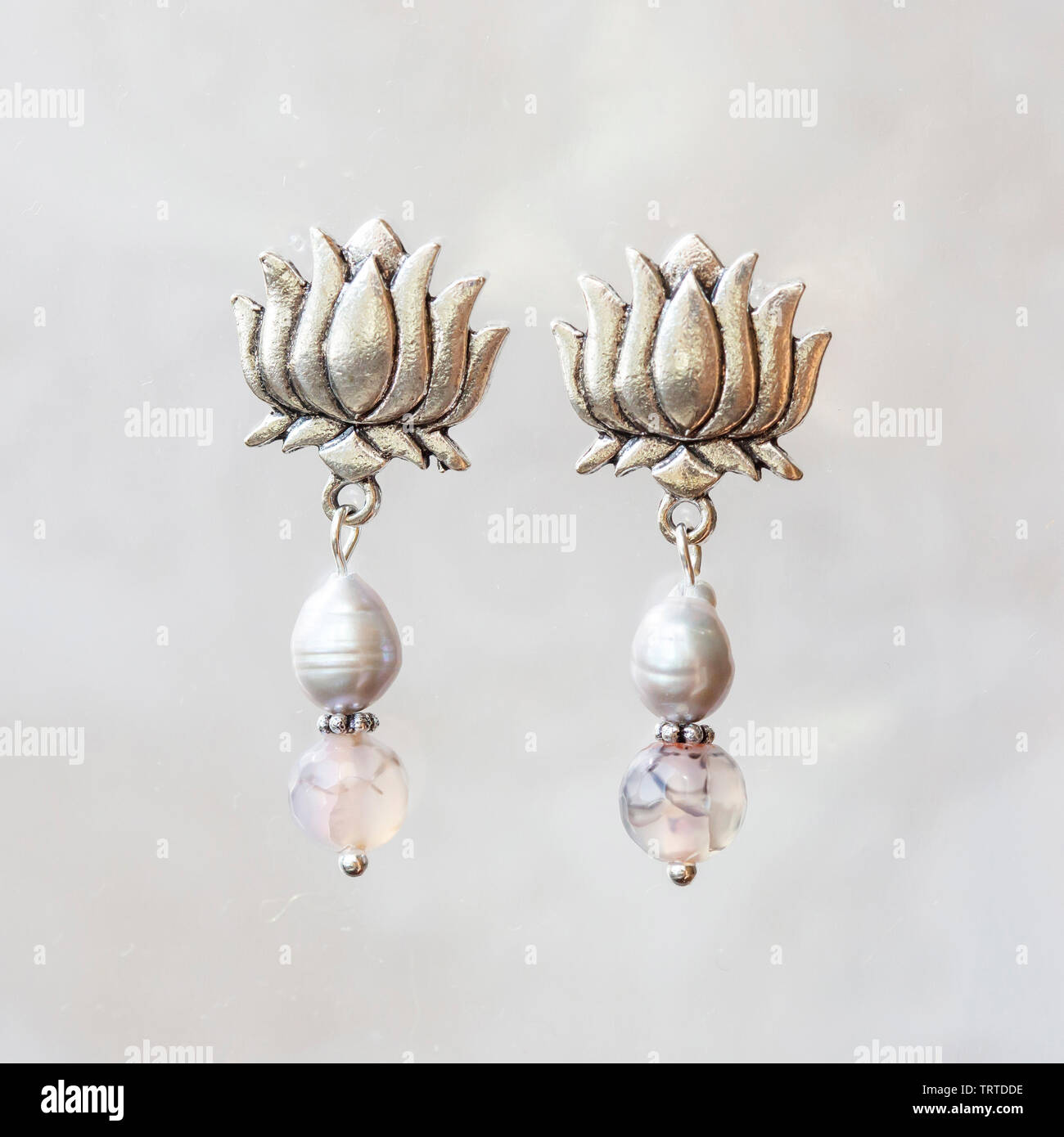 Mineral stone agate and pearl beads lotus shape earrings on neutral background Stock Photo