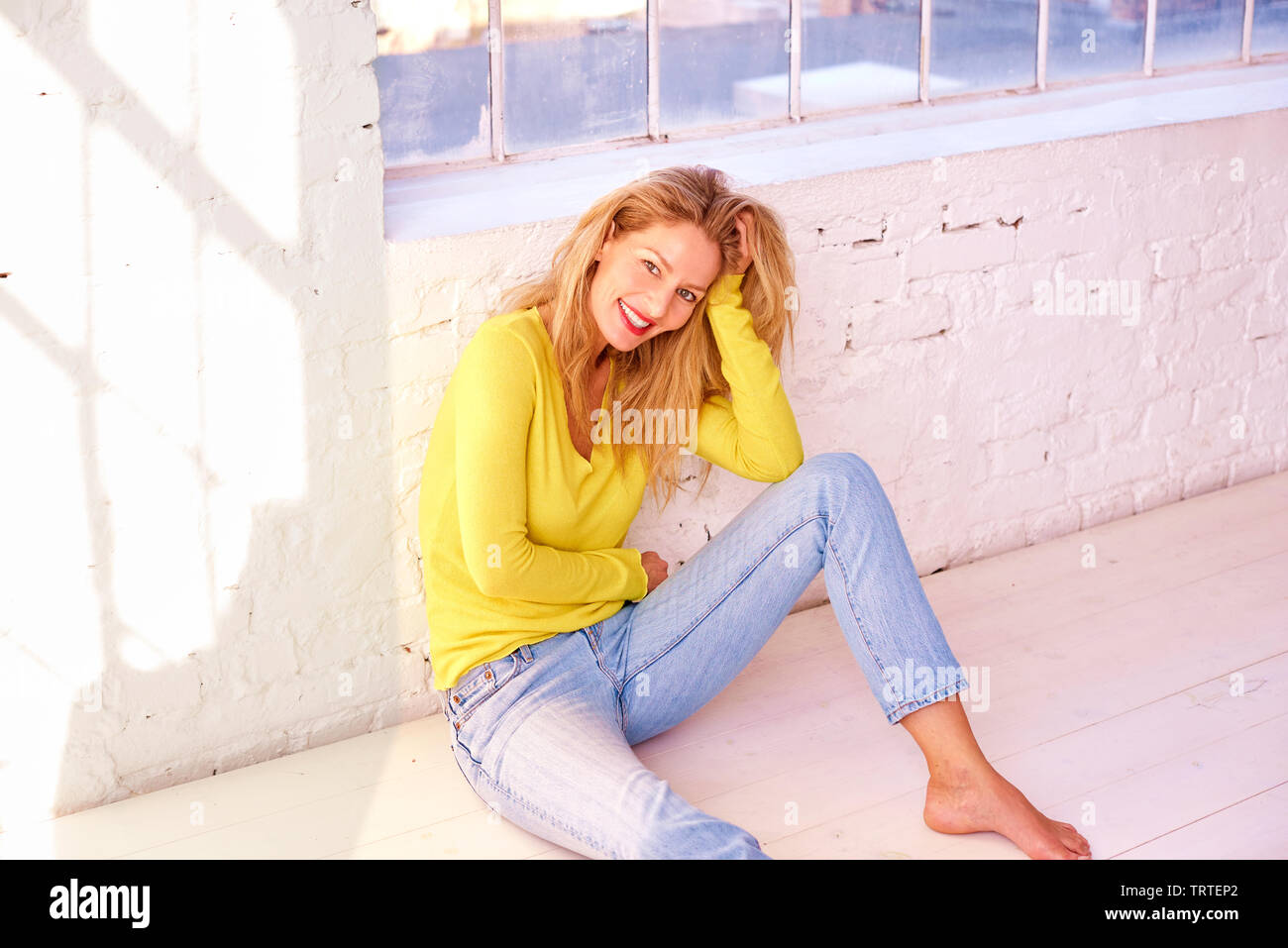 Portrait of beautiful blond woman sitting on the floor and laughing ...