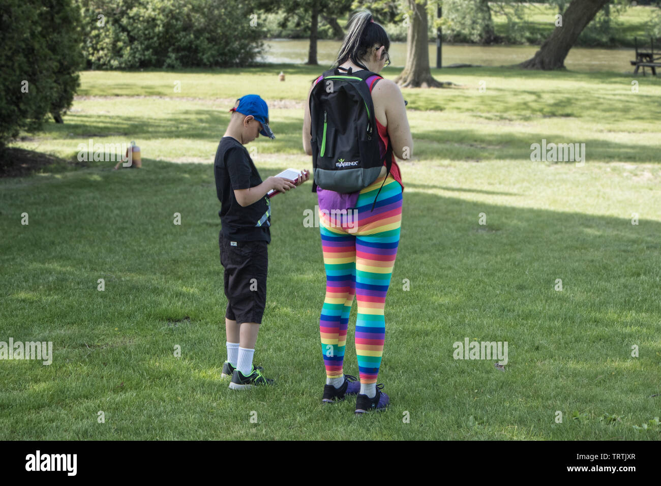 Adult female, oddly dressed with colourful horizontal stripes and a young boy. Both are consulting electronic devices. Stock Photo