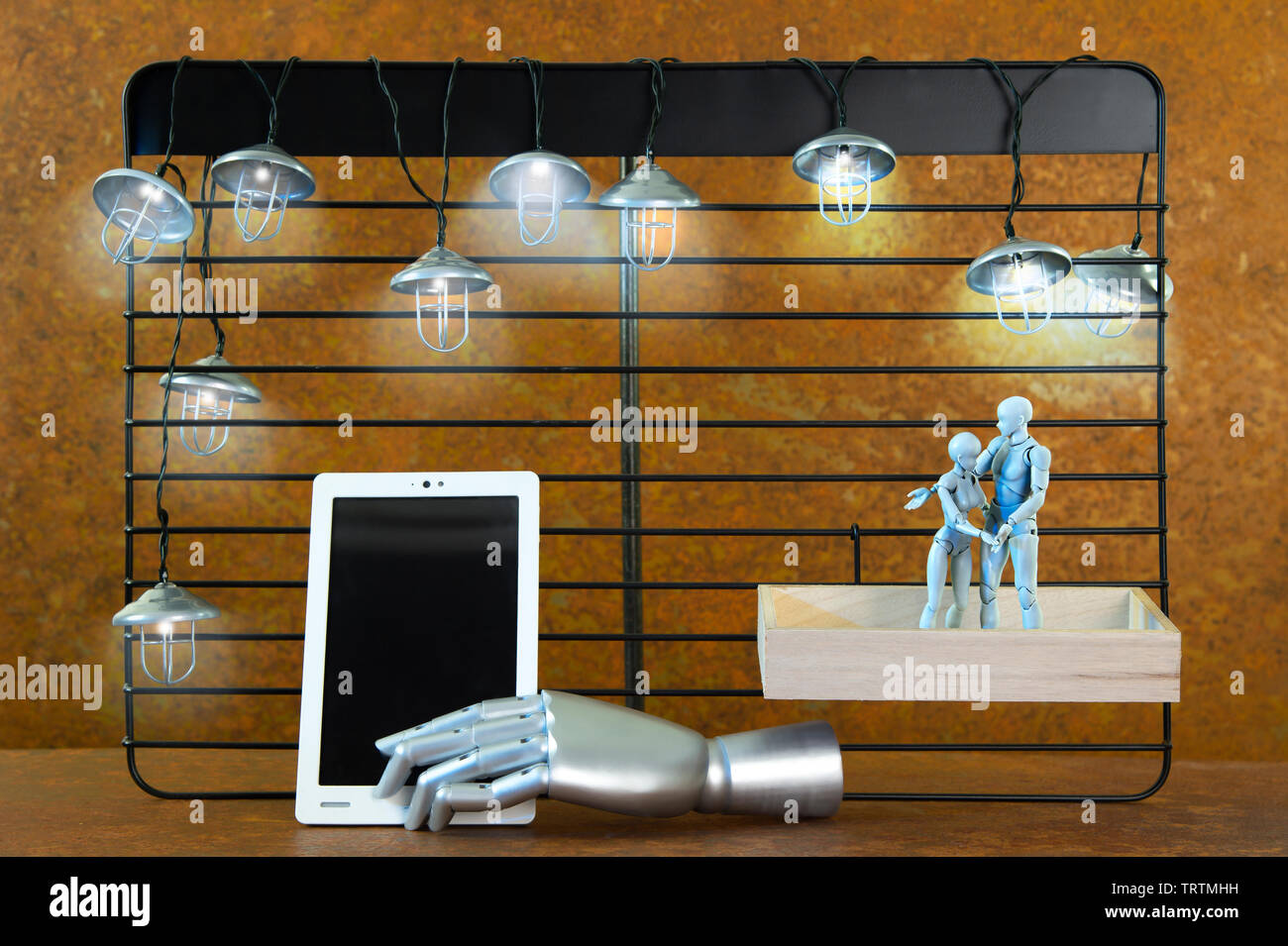 A black shelf in front of real rust. Mine lights shine. Two robot figures hugging each other. The man points to a tablet. A free space on a tablet lea Stock Photo