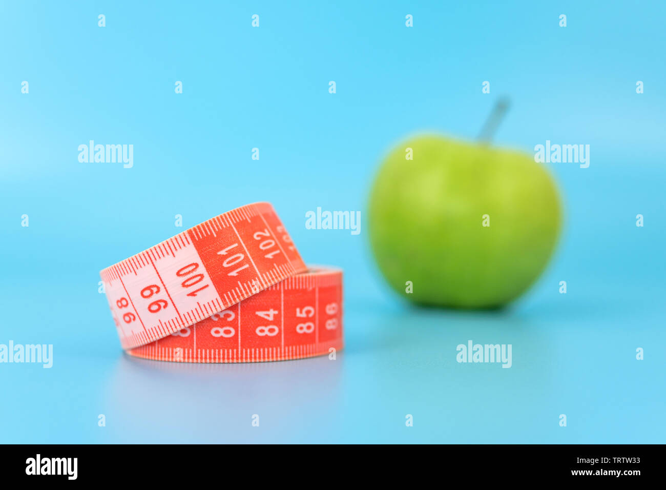 red measuring tape with an apple in the background. concept of excess weight and the concept of weight loss. Stock Photo