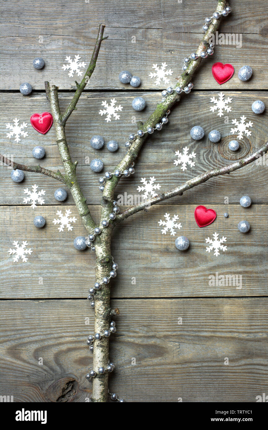 Christmas tree concept with leafless tree branches, snow flakes, red hearts, silver glitter globules and silver bead chain on wooden background Stock Photo