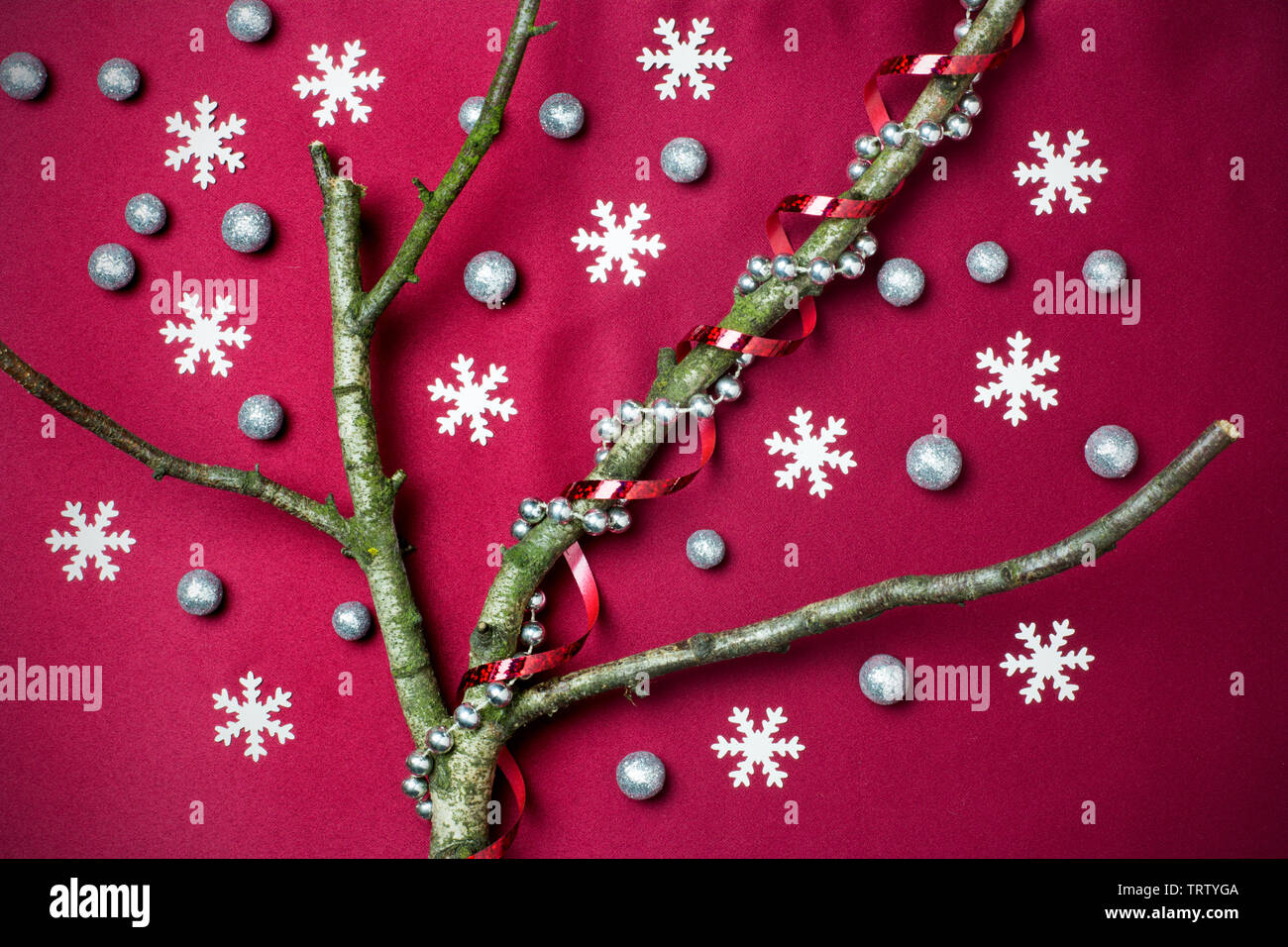Christmas tree concept with leafless tree branches, snow flakes, glitter globules, red ribbon and bead chain on red background Stock Photo