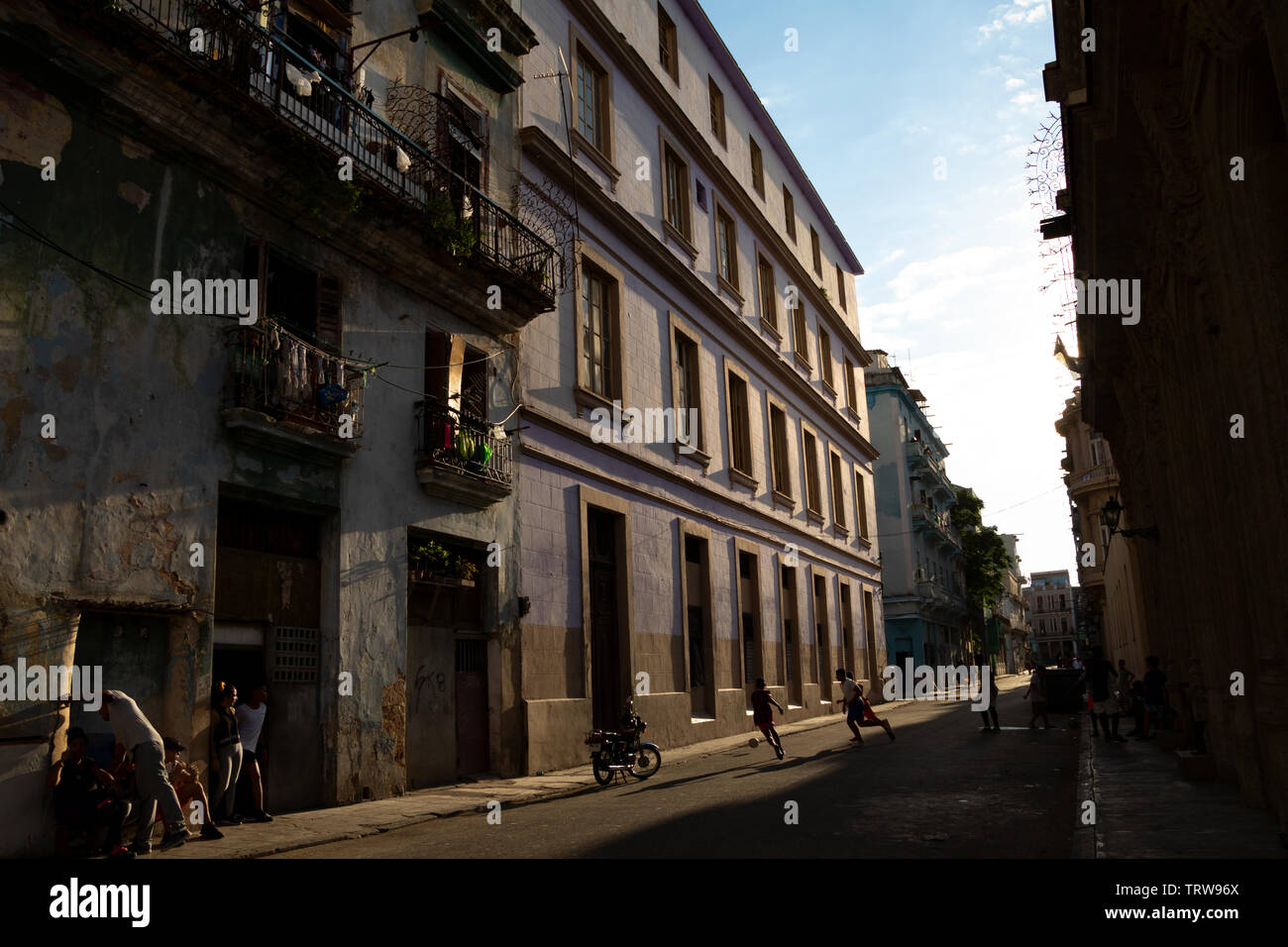 03/26/2019 Havana, Cuba, Street scene in the evening light with boys playing football and adults chatting outside their houses Stock Photo
