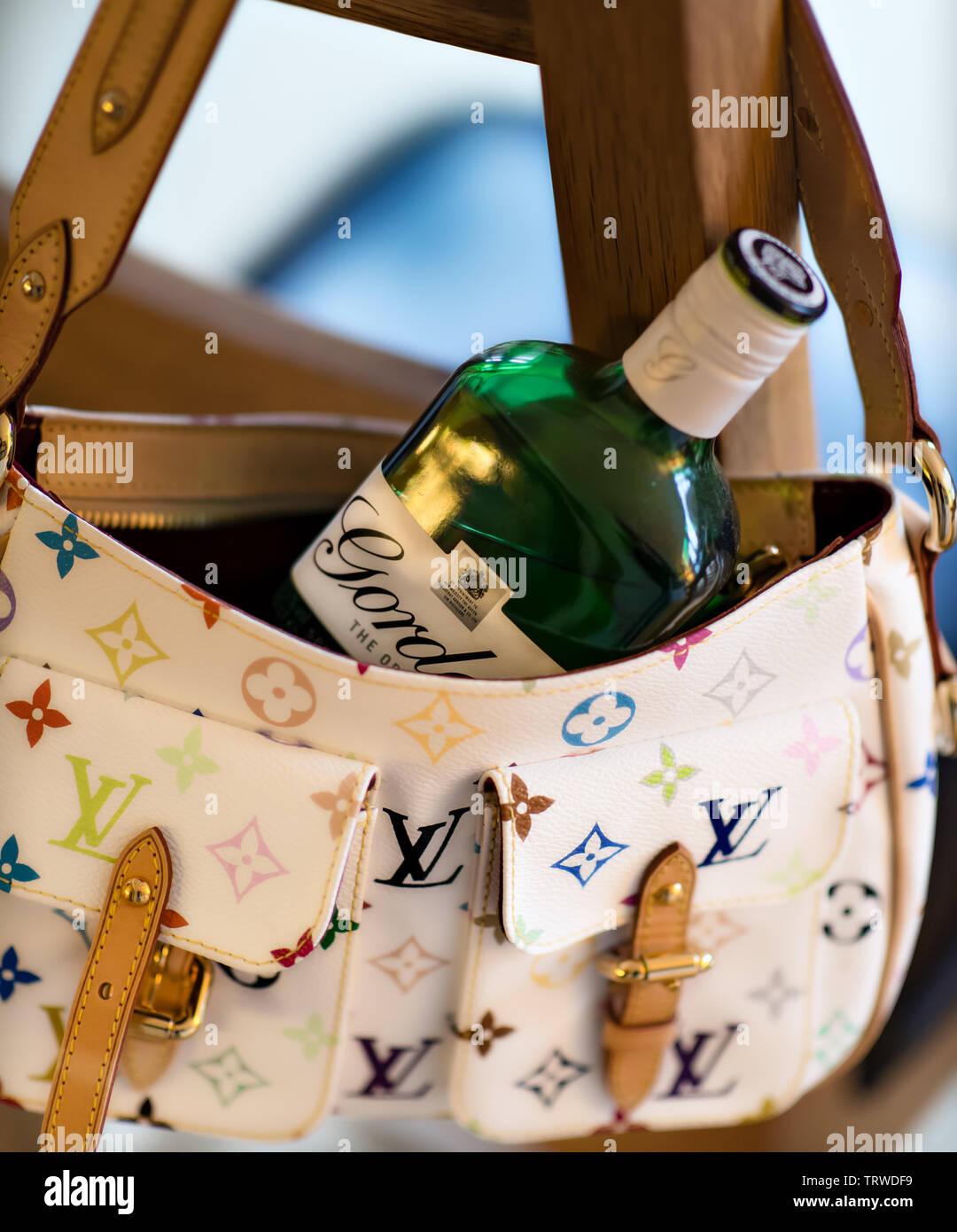 Iconic white Louis Vuitton handbag with a bottle of Gordon's gin hanging on a wooden chair Stock Photo