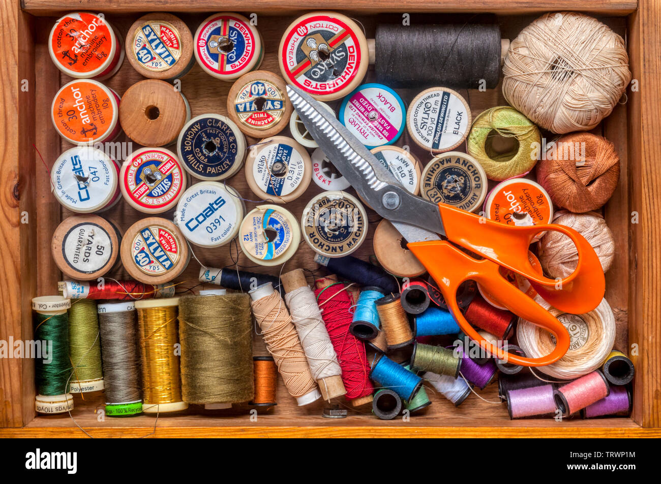 Haberdashery or sewing items stored in a drawer - reels of cotton and thread with a pair of scissors. Stock Photo
