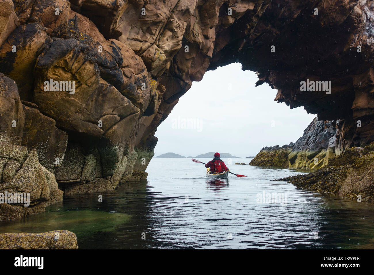 Sea kayaking through a natural arch around the Summer Isles, Wester Ross, Highlands, Scotland Stock Photo
