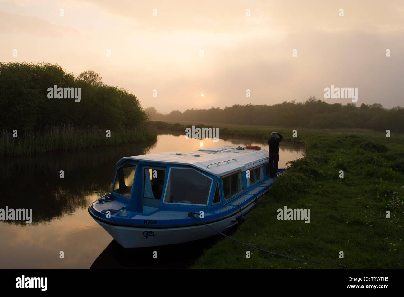 Man on holiday on deck of pleasure craft boat watching a sunset on the River Ant, The Norfolk Broads, UK, May. Stock Photo