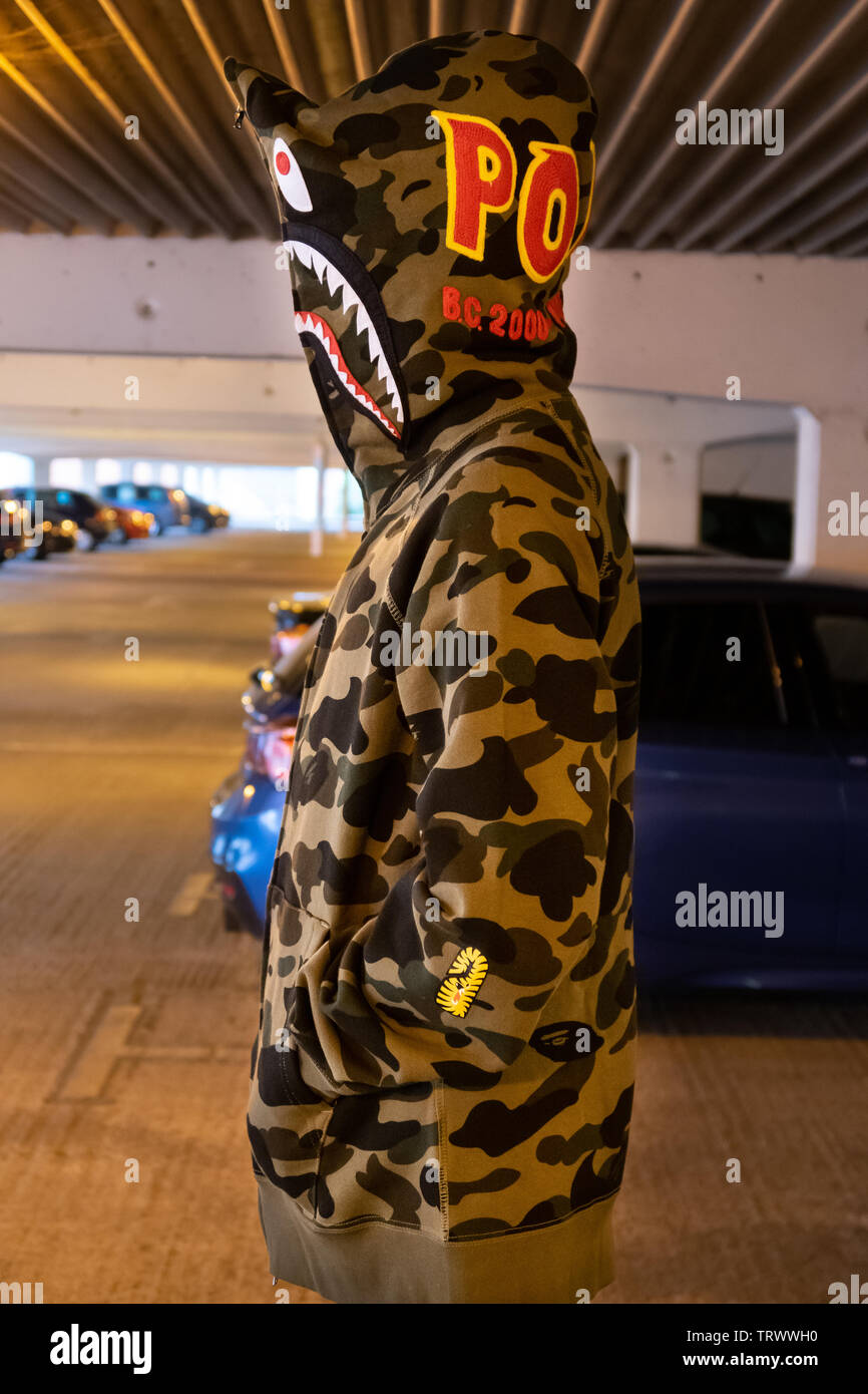 Youth wearing a designer BAPE camo shark hoodie jacket in a dimly lit  multistory car park Stock Photo - Alamy