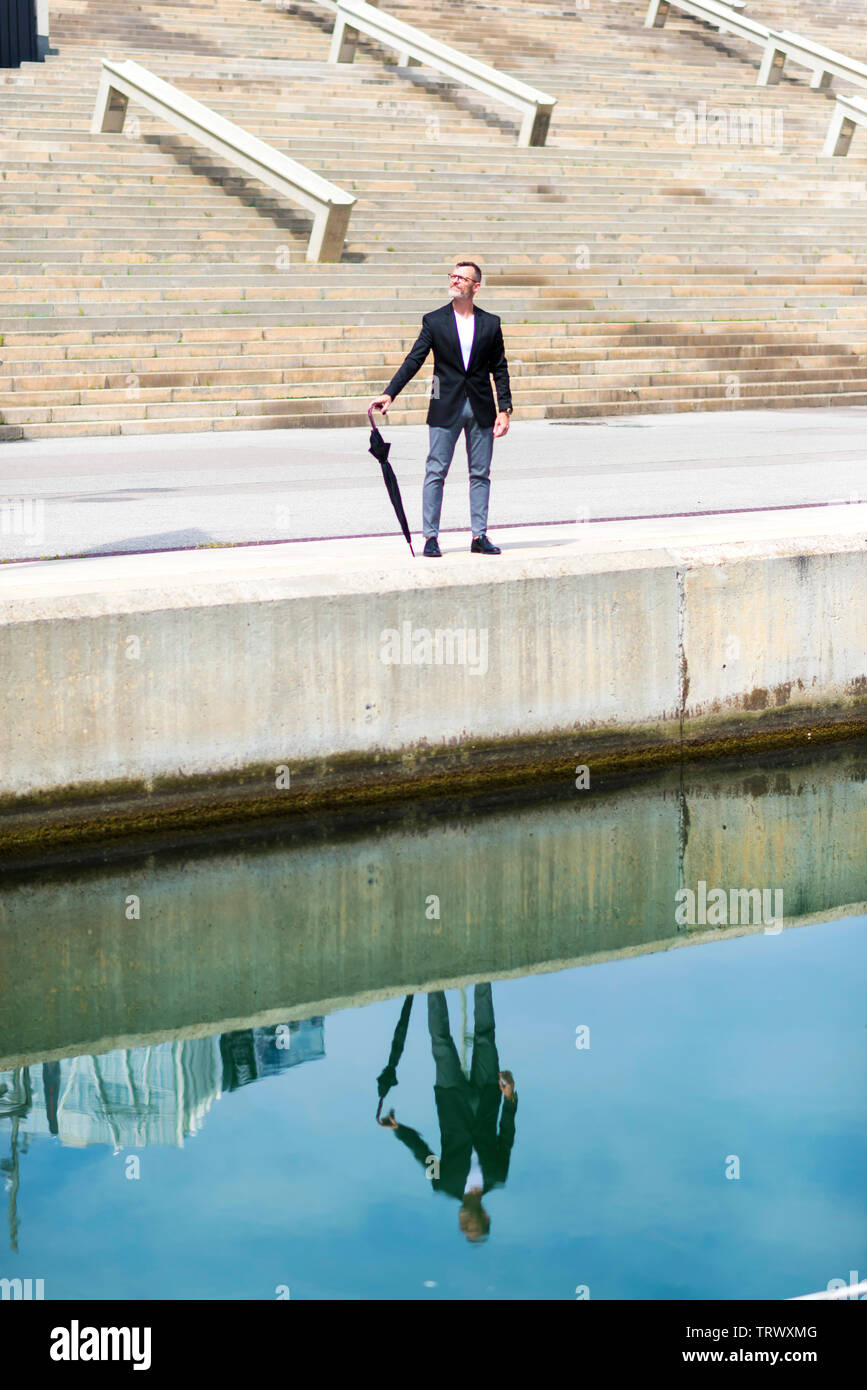 Adult man in formal clothes while walking on promenade holding an umbrella. Stock Photo