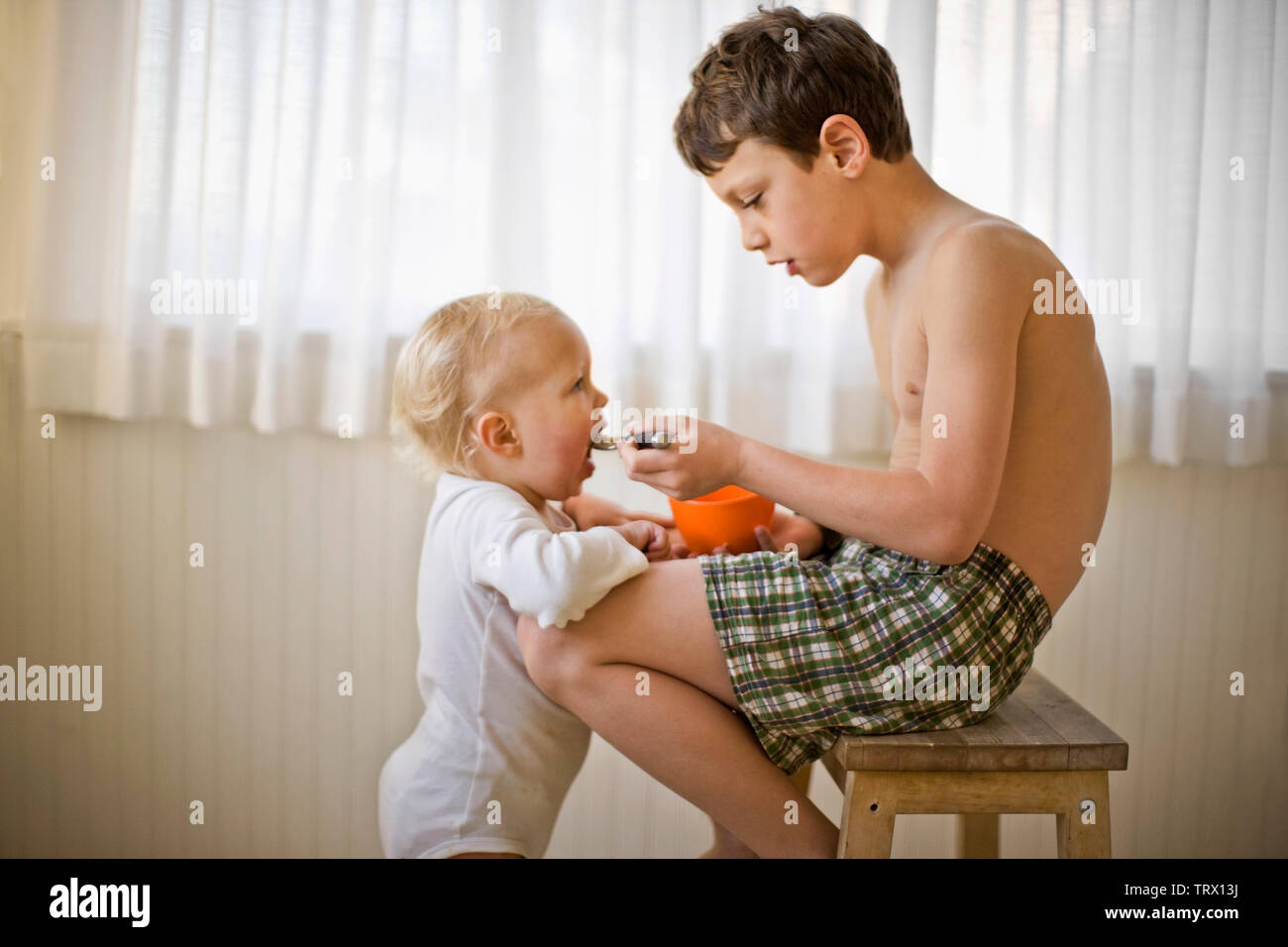 shirtless boy brother sitting feeding alamy stool spoon while