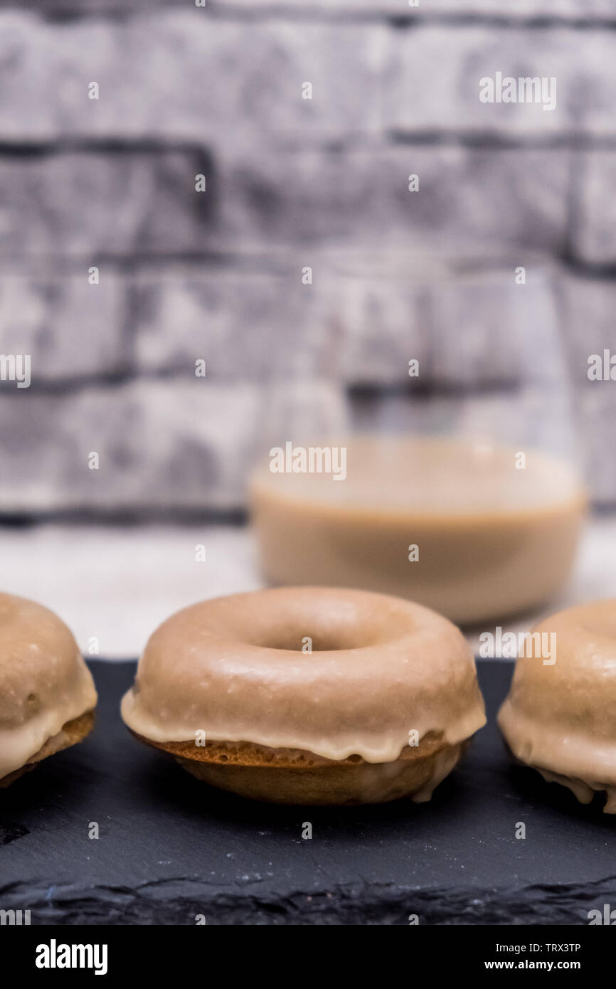 Golden Ginger Doughnuts Dipped in Irish Cream Glaze with a Glass of Irish Cream Behind and a Textured, Grey Brick Background Stock Photo