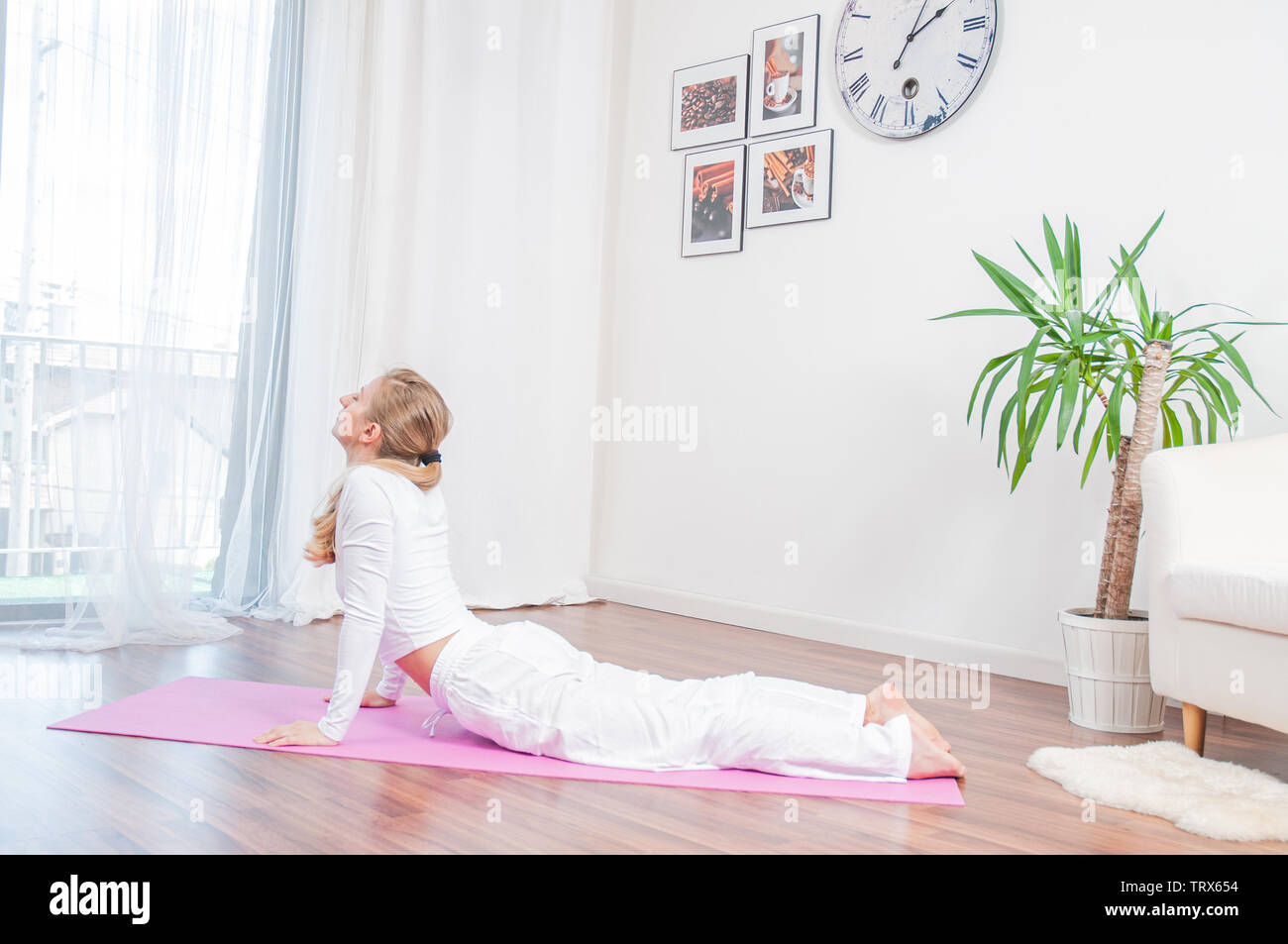 Yoga time. Young woman is practicing yoga at home on yoga mat, doing ...