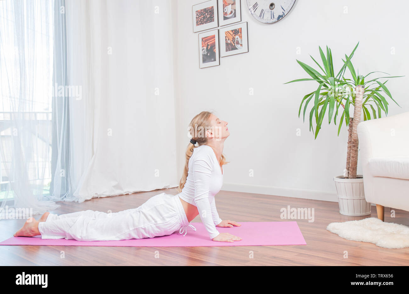 Yoga time. Young woman is practicing yoga at home on yoga mat, doing ...