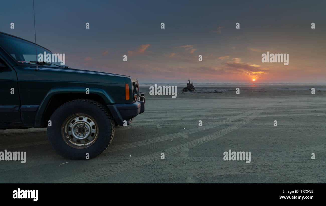 green SUV on the beach with a sunset Stock Photo