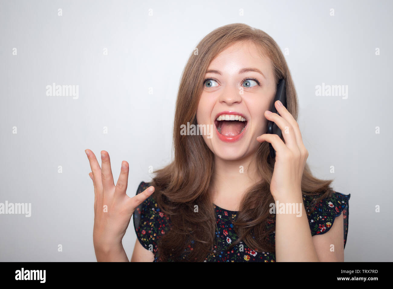 Young caucasian woman with mobile phone looks excited to hear good news Stock Photo