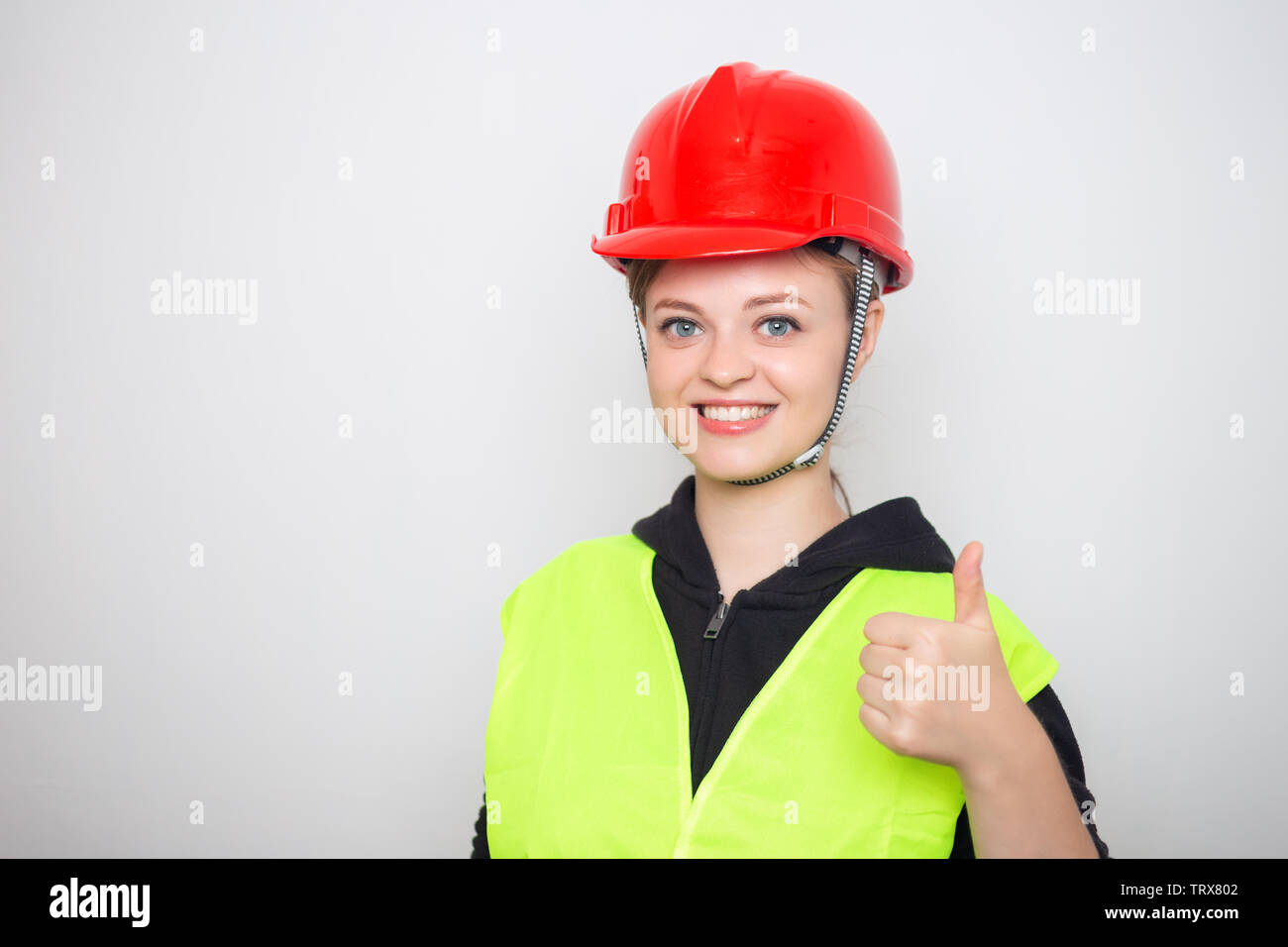 Young caucasian woman wearing red safety hard hat and reflective vest, smiling with thumbs up Stock Photo