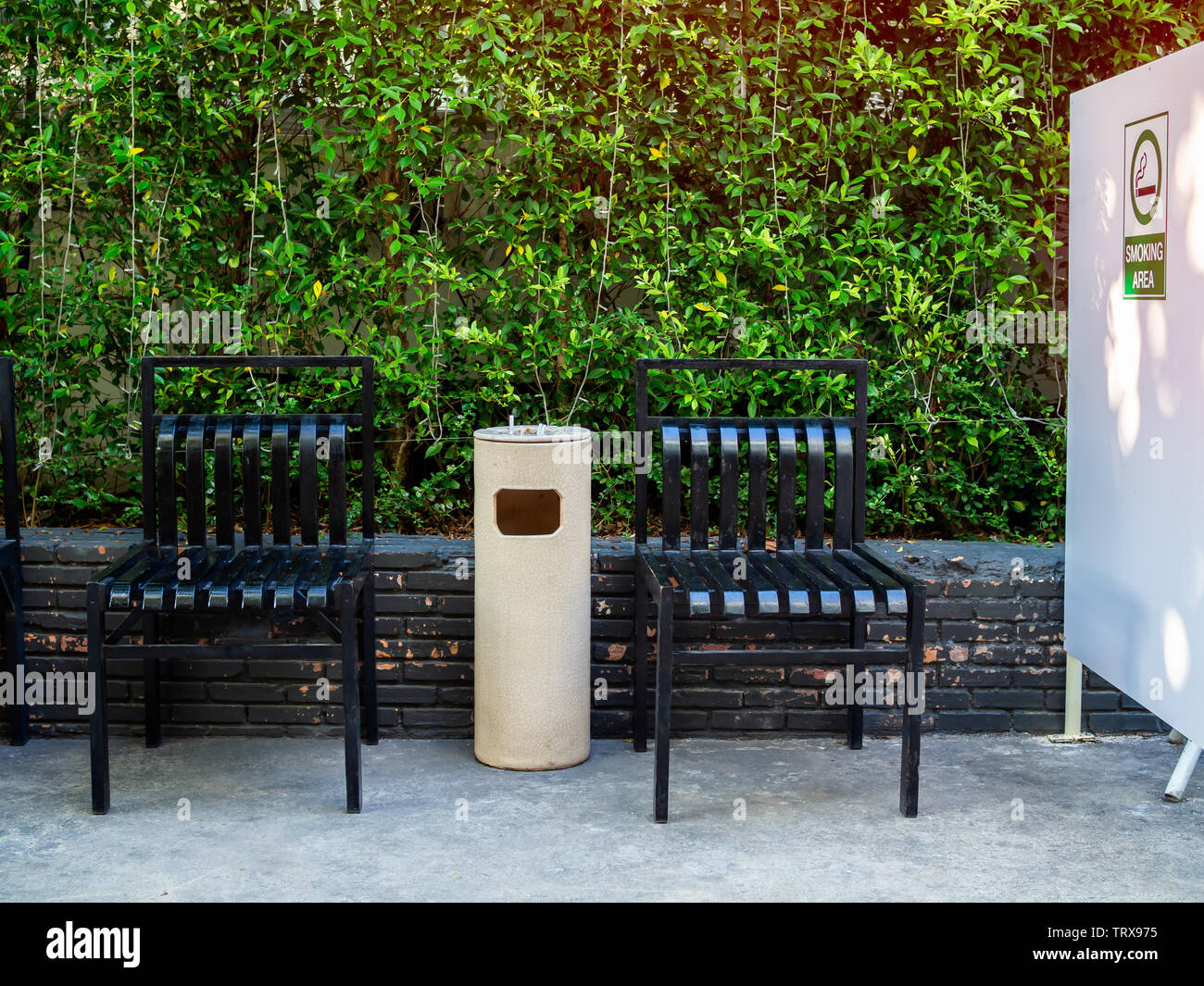Two black chairs with ashtray in smoking area on green garden