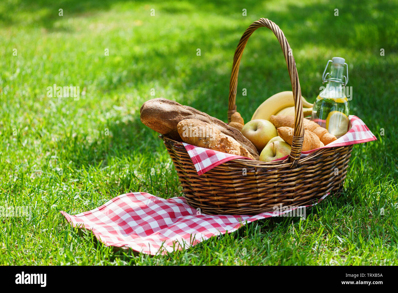 Wicker picnic basket with food and drink in a park. Summer picnic on the grass or lawn. Stock Photo