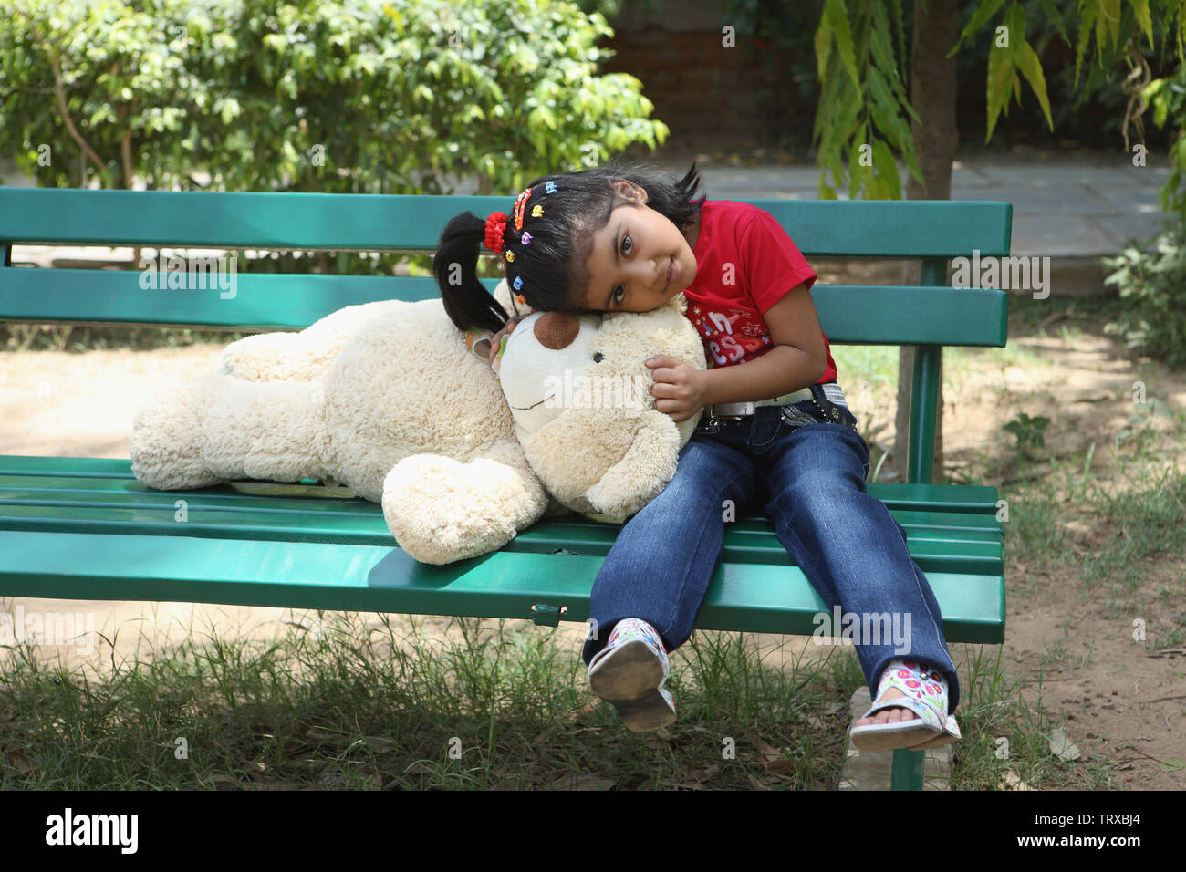 Girl with a teddy bear sitting on a bench Stock Photo - Alamy