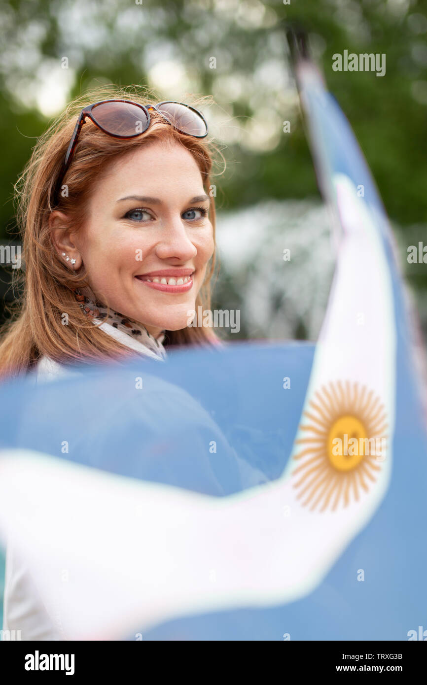 Happy young natural woman holding flag of Argentina in park, depth of field Stock Photo
