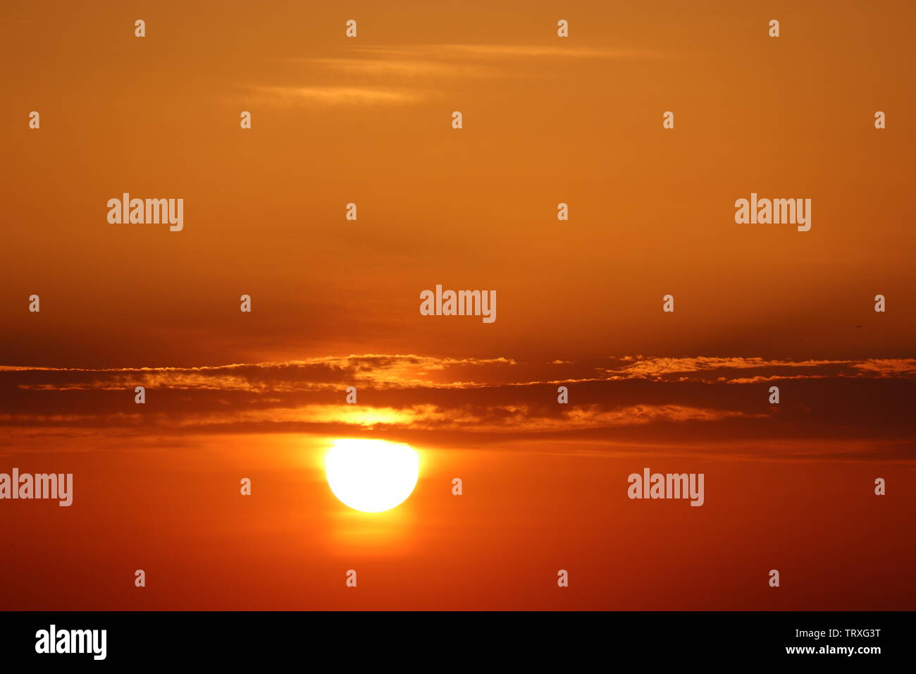 Sunset with clouds, setting shining sun and orange evening sky. Beautiful skyline for background Stock Photo