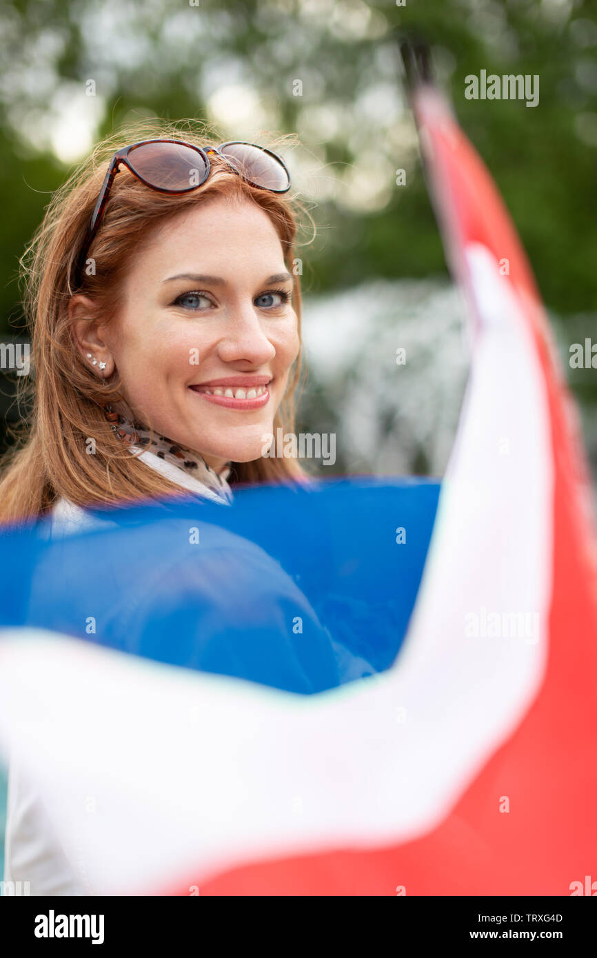 Happy young natural woman with smile holding flag of Netherlands in park, depth of field Stock Photo