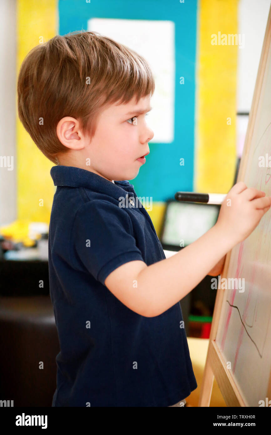 Child is drawing and painting with felt pen on paper of wooden drawing