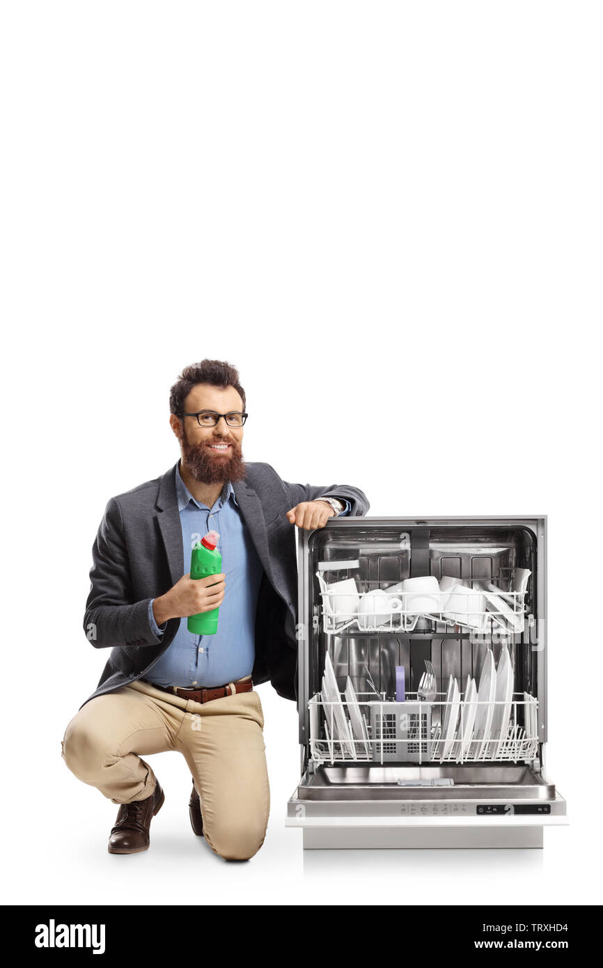 Man kneeling next to a dishwasher and holding a bottle of washing cleaning supply isolated on white background Stock Photo