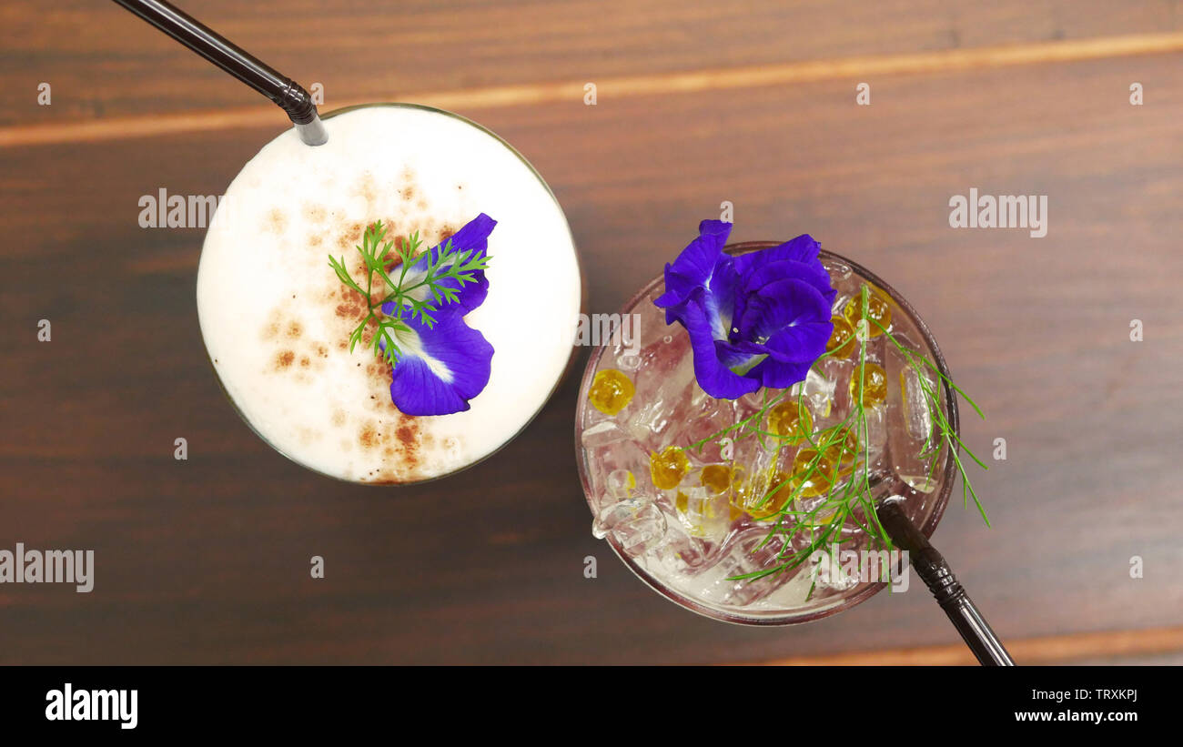 two glasses of drink, coffee and italian soda menu on the table at coffee shop decorate with pea flower and green grass Stock Photo