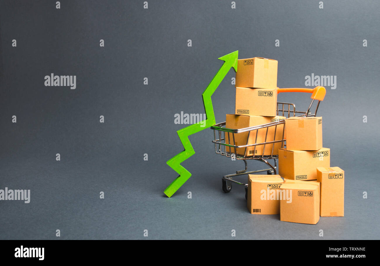 Shopping cart with cardboard boxes and a green up arrow. Increase the pace of sales and production of goods. Improving consumer sentiment, economic gr Stock Photo